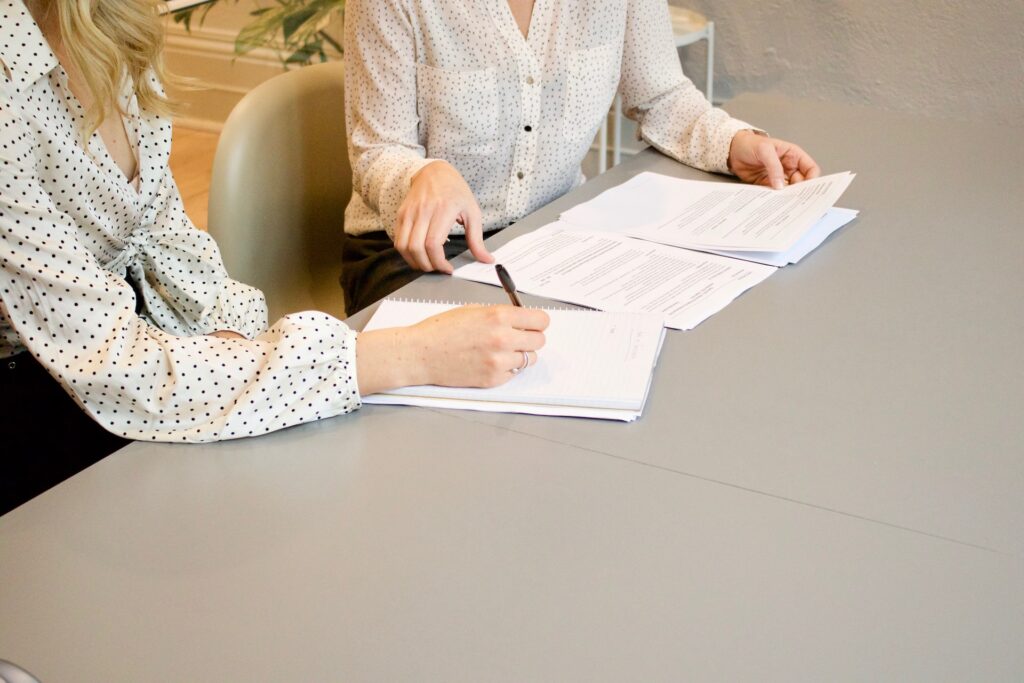 Two people sitting at a desk signing lease agreement documents with a pen in a modern office setting.
