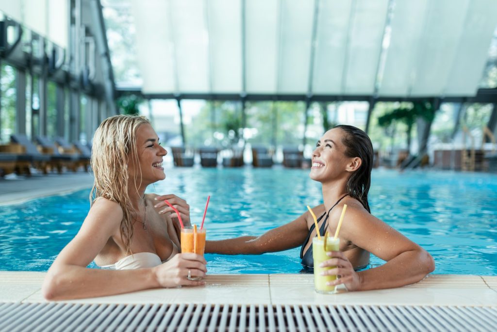 Two women in a swimming pool on vacation enjoying the benefits of their digital real estate investments.