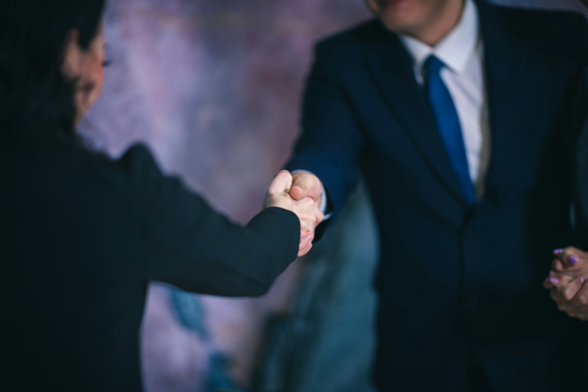 A real estate agent shaking hands with a landowner in front of a "For Sale" sign on a vacant plot of land