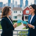 Two female real estate investors standing in front of a house in suburban Chicago discussing purchasing the home as a rental investment.