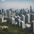 A sunny city skyline with various properties, including office buildings, residential complexes, and commercial spaces, surrounded by greenery and a bustling street below