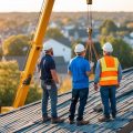 Two real estate investors standing in front of their rental property watching workers replace the roof using a crane.