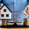 A person comparing a house and a stack of money, with a scale in between