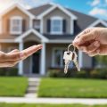 A seller handing over a set of keys to a buyer in front of a real estate property