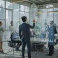 A group of real estate professionals working together in an office with a large digital screen showing property data and graphs.