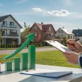 A person reviewing property data outdoors in a residential neighborhood with houses and a rising bar graph symbolizing real estate value growth.