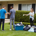 A landlord taking house keys from two tenants leaving their rental property with their belongings piled on the front lawn.