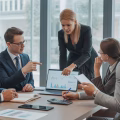 A group of business professionals discussing documents and a laptop in a bright real estate office.