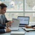 Three business professionals reviewing legal documents and property reports around a conference table in an office.
