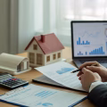 Person reviewing financial documents and calculator on a desk with a house model nearby.