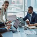 Four professionals in a business meeting discussing real estate investment around a conference table with laptops and documents.
