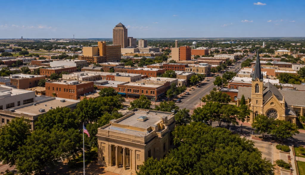 Aerial view of a West Texas downtown with historic brick buildings, church steeple, civic architecture, and flat plains beyond the city.