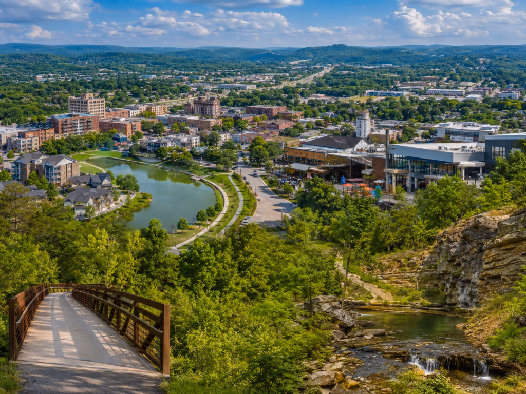 Northwest Arkansas metro view with a walkable greenway, creek, rocky overlook, and a growing mixed-use district.