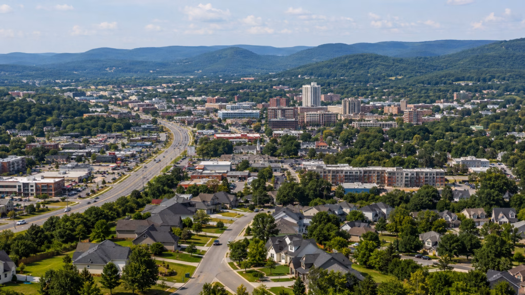 Aerial view of the Fayetteville-Springdale-Rogers area with suburban neighborhoods, commercial corridors, downtown buildings, and Ozark hills.
