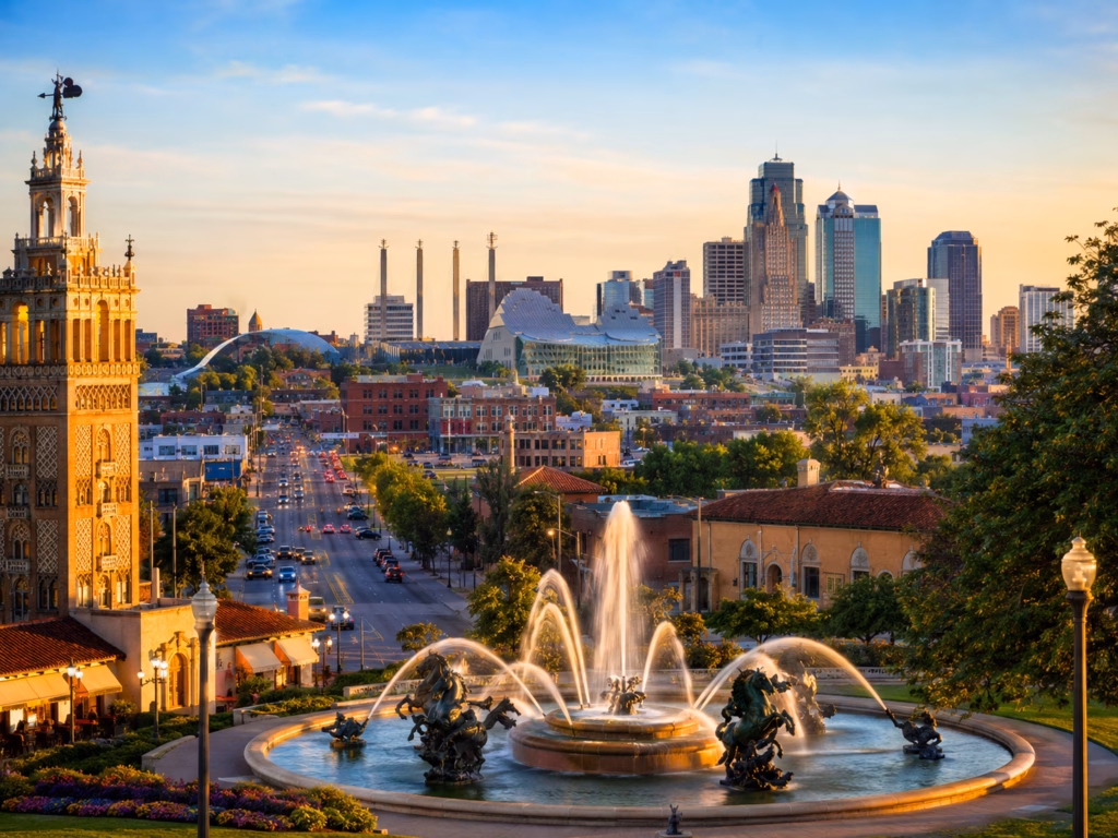 Kansas City skyline at golden hour with a grand fountain, historic architecture, and a broad avenue leading into downtown.