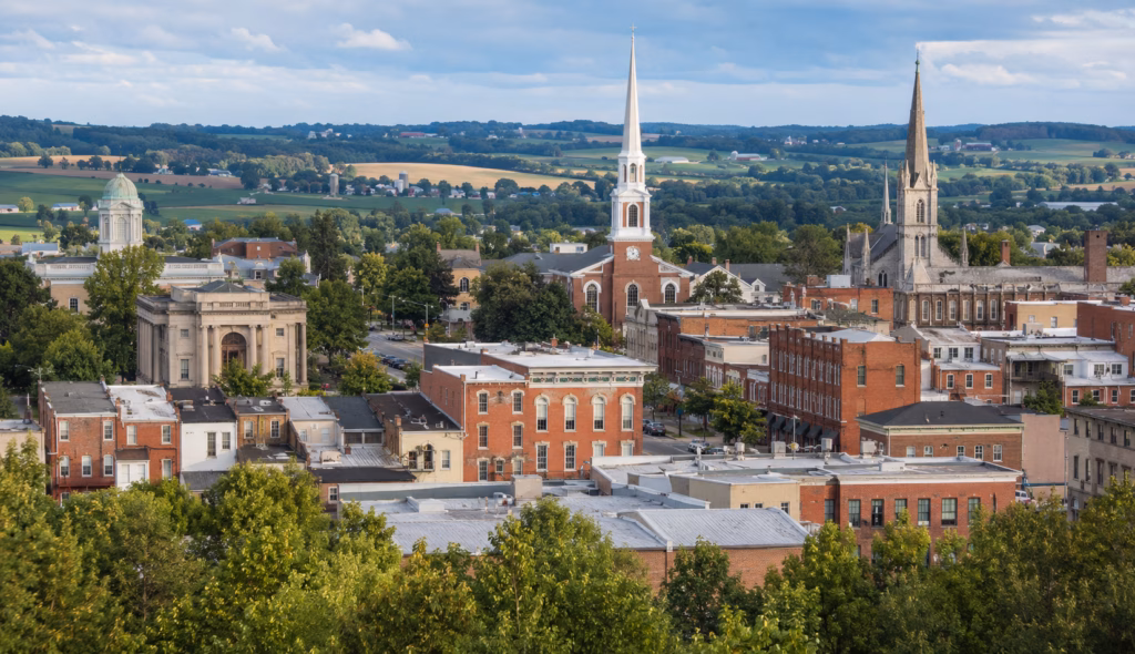 Small Pennsylvania town skyline with historic brick buildings, church steeples, courthouse-style architecture, and farmland beyond.