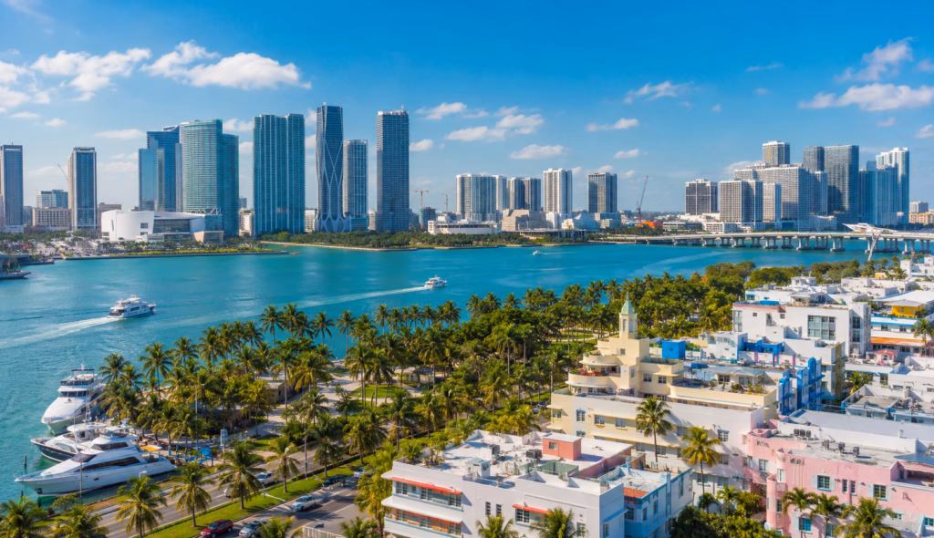 Miami waterfront skyline with Biscayne Bay, palm trees, yachts, Art Deco-style buildings, bridges, and modern high-rise towers.