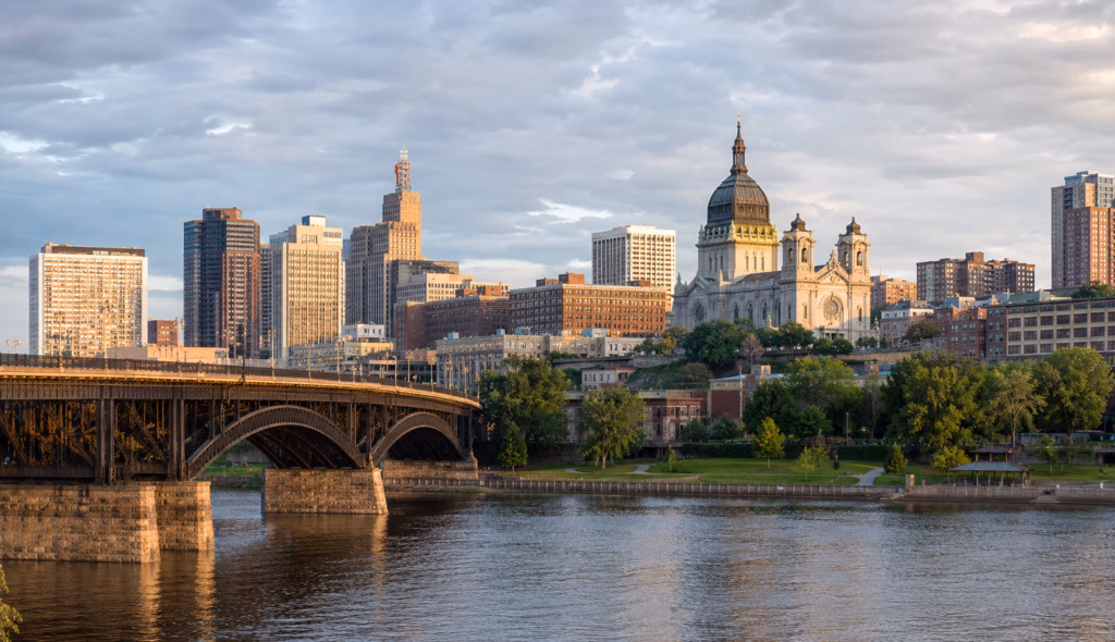 Downtown skyline along the Mississippi River with bridges, historic civic buildings, high-rises, and riverfront green space.