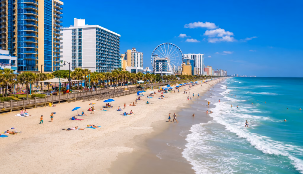 Wide sandy beach with oceanfront hotels, turquoise water, beachgoers, palm trees, and a large Ferris wheel along the shoreline.