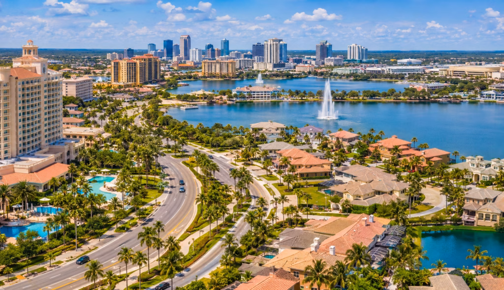 Aerial view of Central Florida with resort hotels, lakefront homes, palm-lined roads, fountains, and a distant urban skyline.