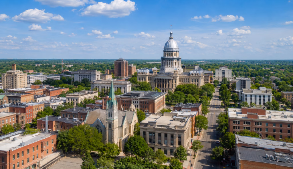 Downtown Springfield skyline with the Illinois State Capitol dome, historic buildings, tree-lined streets, and civic architecture.